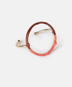 The DIP DYE BRACELET by MOMONI is a uniquely designed artisanal piece, featuring an enamelled metallic golden band with a round, circular structure. The bracelet showcases an elegant combination of half brown and half light blue hues, boasting an irregular, organic shape and minimalist style, set against a plain white background.