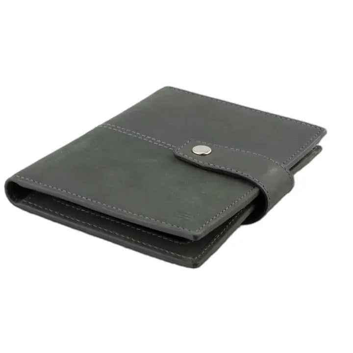 The GARZINI RFID-blocking leather passport holder in Carbon Black features multiple card slots, a pen holder, angled pockets, a transparent ID window, an Airtag compartment, and a snap-button closure flap.
