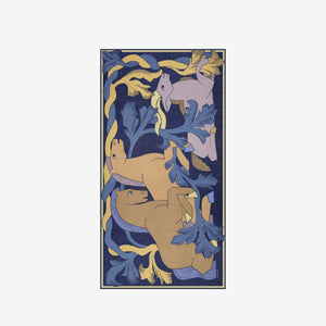 A woman stands against a white background, wearing a cream jacket, beige pants, and INOUI EDITIONS’ Cavale Horse Wool Scarf in Navy—hand-printed in India with a vibrant unicorn design—draped over her neck and shoulder.