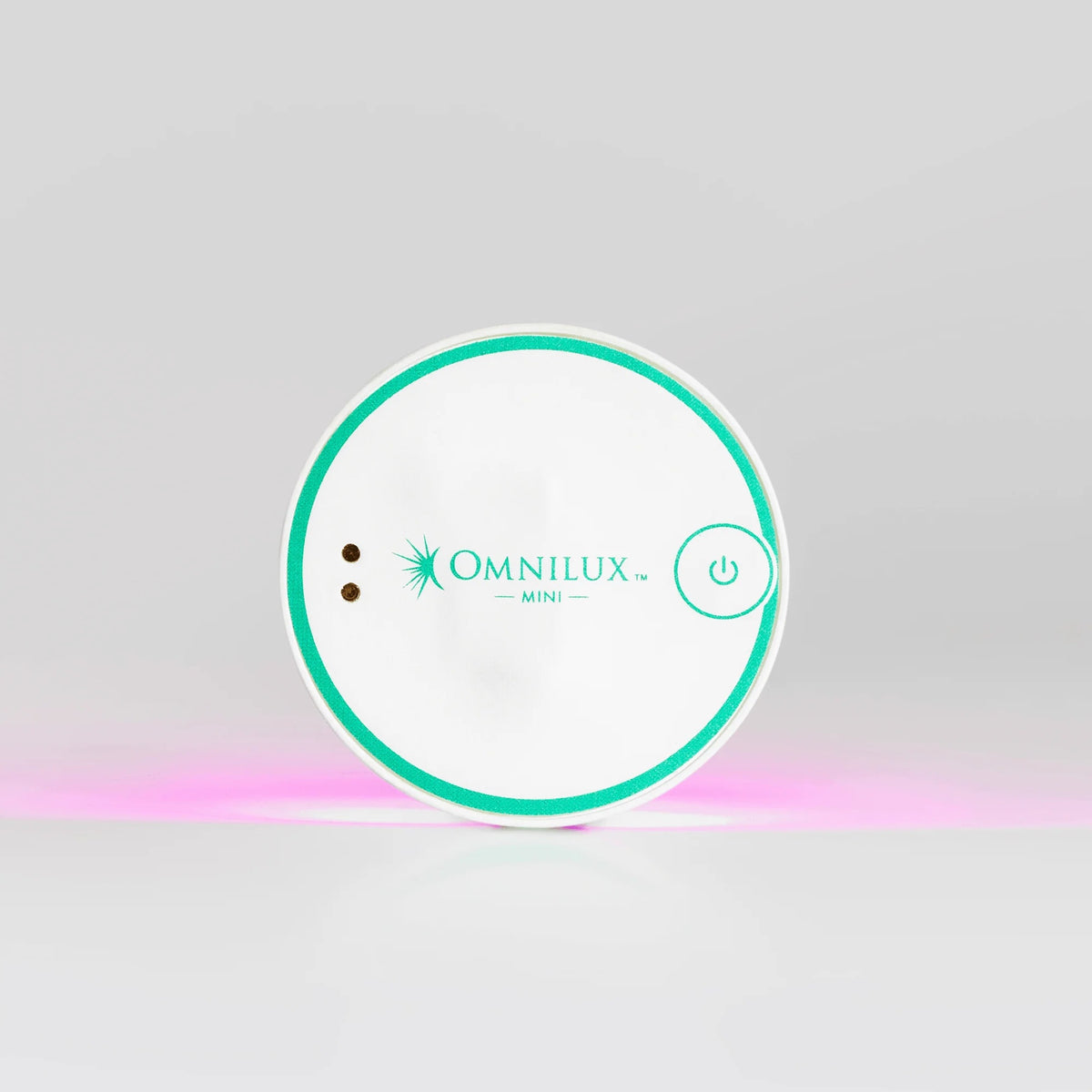 A round, white OMNILUX - BLEMISH ERASER KIT device from OMNILUX features a teal rim, power button, and logo; a soft pink light glows from underneath, showcasing its advanced blue and red light therapy technology.