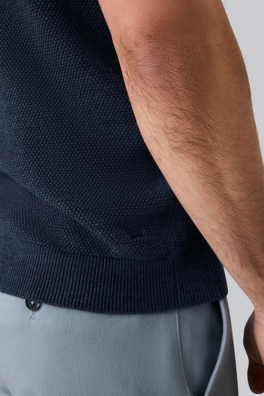 A man with short dark hair is seen from behind wearing the MACK WELDON Tech Linen Johnny Collar Polo Sweater in Sage Leaf Heather, paired with light gray pants against a plain light gray background.