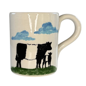 The FEARRINGTON SIGNATURE COLLECTION - BELTIE MUG BY VIETRI features painted black and white cows on green grass under blue clouds.