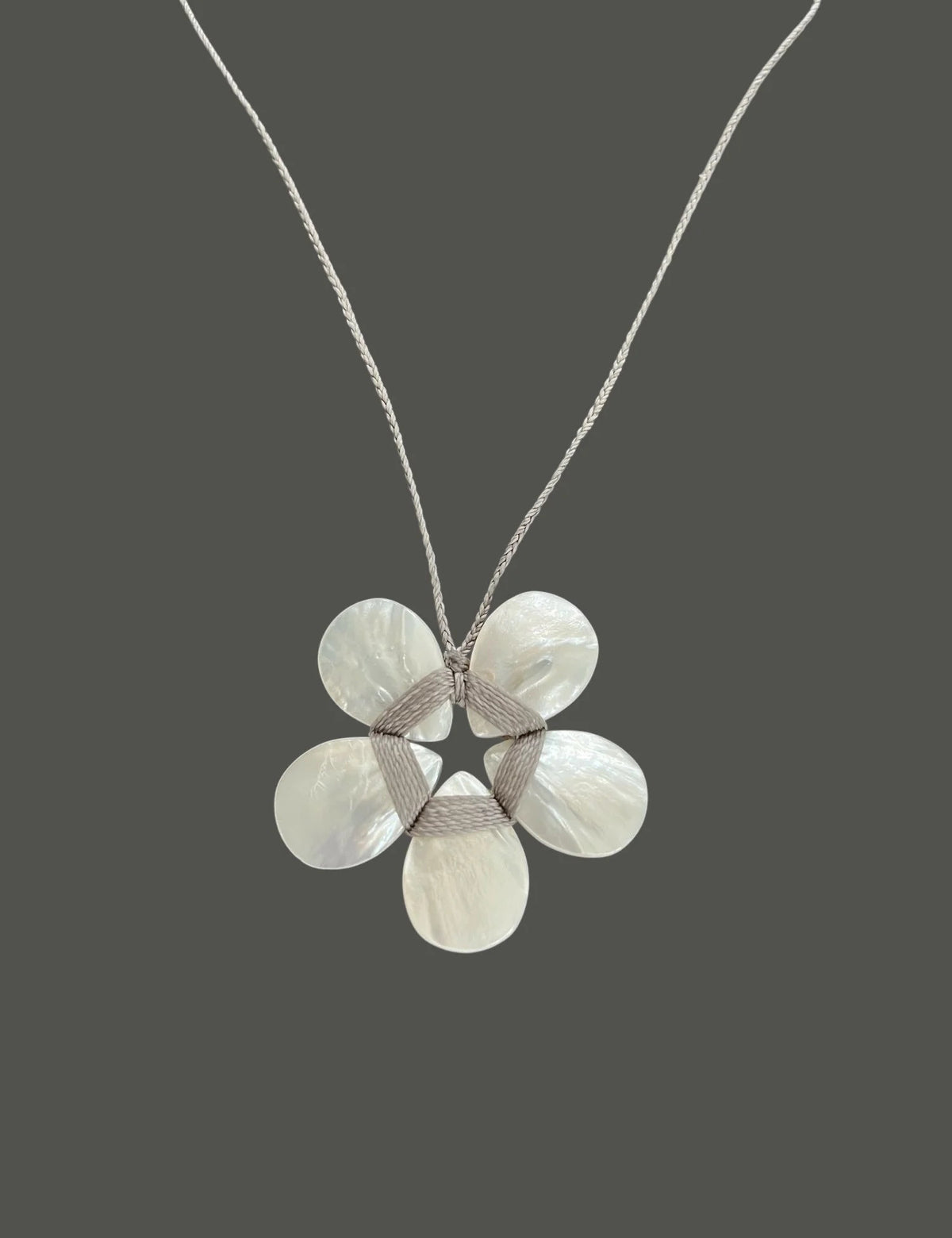 The ANN LIGHTFOOT MOTHER OF PEARL FLOWER NECKLACE features a five-petal flower pendant made from iridescent white shell pieces, strung on a delicate, adjustable braided gray thread necklace.