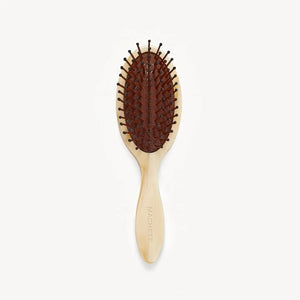 The MACHETE - Petite Travel Detangling Hair Brush in Alabaster features an oval head, brown cushioned base, and nylon bristles. The wooden handle is engraved with "MACHETE" and is shown against a plain white background.
