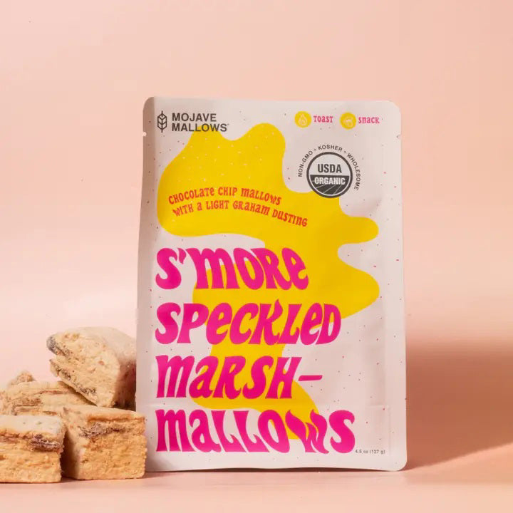 A standing pouch of MOJAVE MALLOWS - S’MORE SPECKLED MARSHMALLOWS by MOJAVE MALLOWS, showcasing bold pink and yellow lettering with playful graphics on a cream background. The packaging emphasizes these organic s’more marshmallows—decadent chocolate chip treats dusted with graham cracker, ideal for anyone seeking artisanal marshmallows with a unique twist.