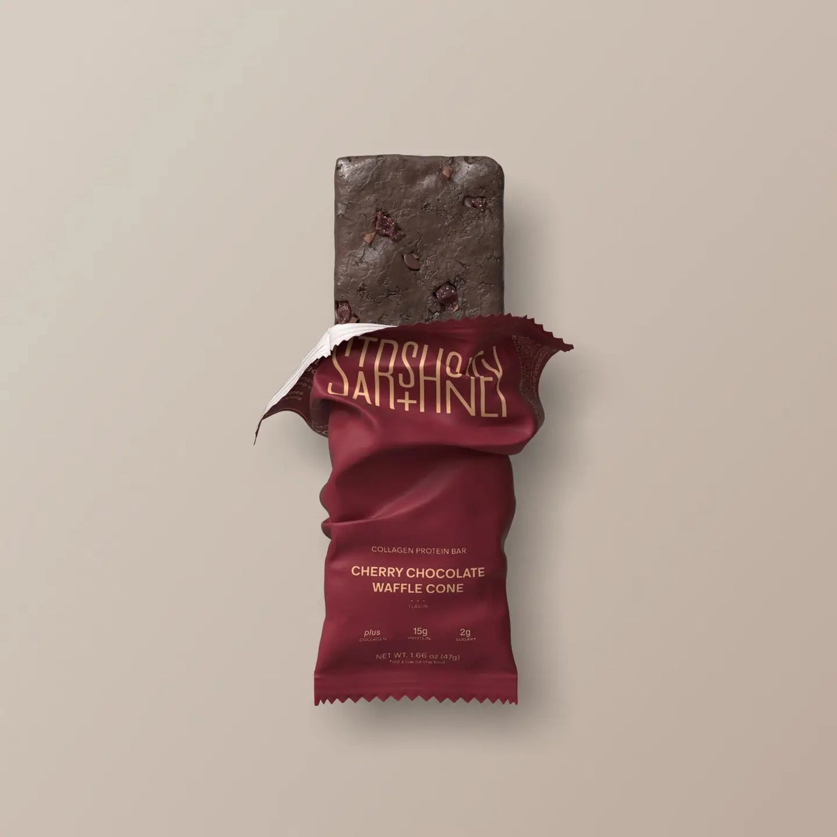 A maroon protein bar wrapper labeled “STARS+HONEY” displays the flavor “CHERRY CHOCOLATE WAFFLE CONE” with nutrition highlights: 8g collagen, 15g protein, and 2g sugar, all set against a beige background. This indulgent treat puts the rich chocolate and tart cherry combination front and center.