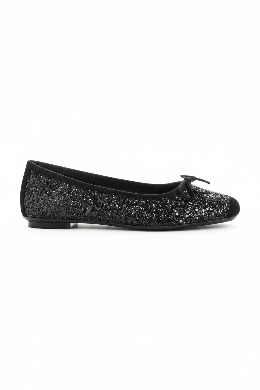 The REQINS Harmony Sequin Ballerina Flats in Noir feature black sequins, black toe caps, and small bows—bringing a touch of everyday luxury against a plain light background.