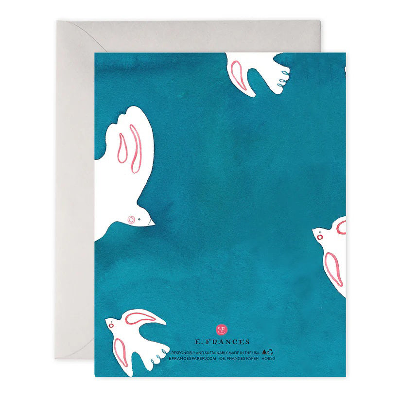 The PEACE DOVES HOLIDAY CARD by E.FRANCES PAPER features a handcrafted watercolor design of lovely white doves holding olive branches on a teal background, with &quot;Peace on Earth&quot; elegantly scripted in gold. This exquisite card is partially nestled inside a light gray envelope and proudly made in the USA.