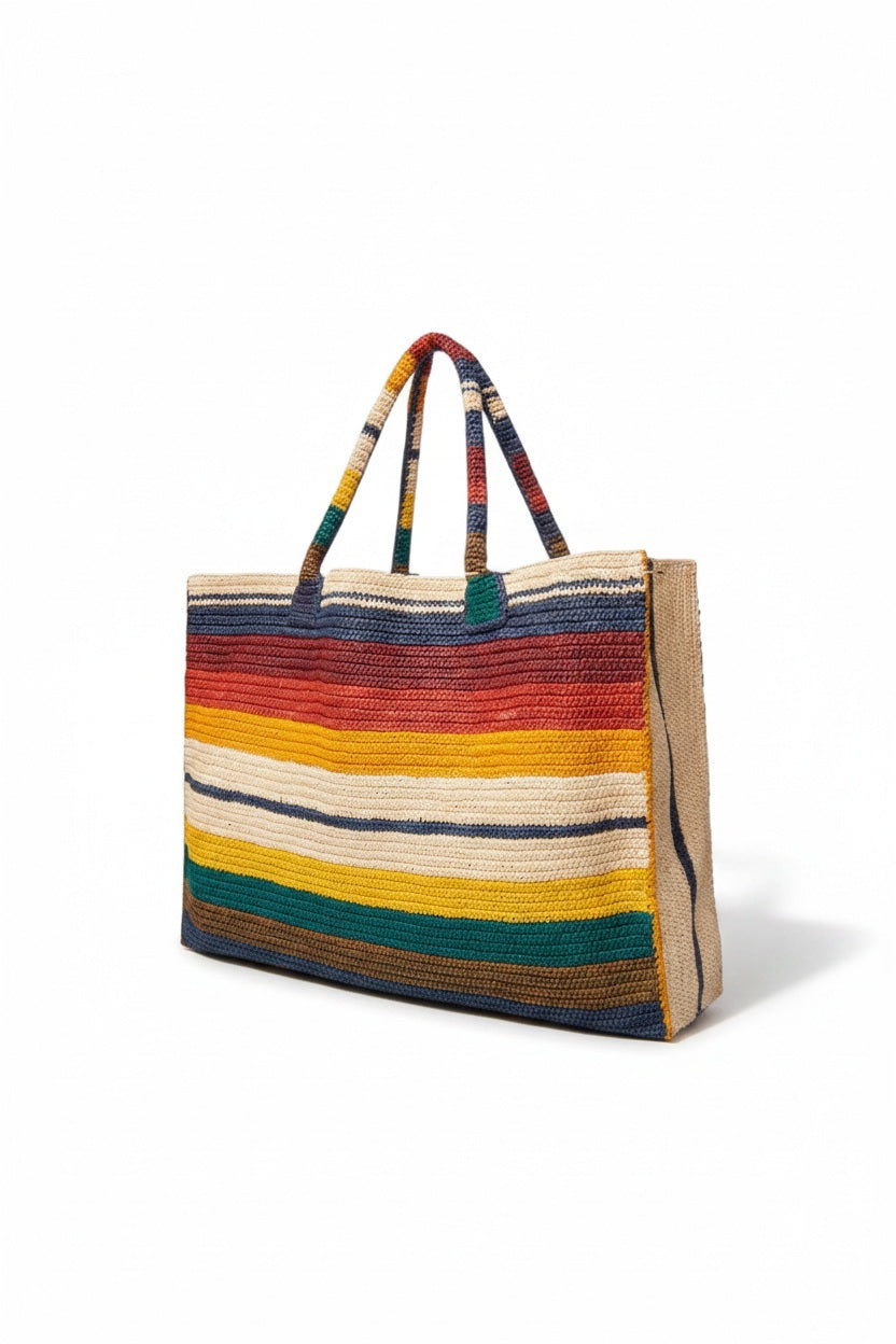 The GABRIELE FRANTZEN Raffia Weekender Bag Horizon is a rectangular, hand-crocheted bag with two handles and horizontal red, navy, cream, yellow, and green stripes on a white background.