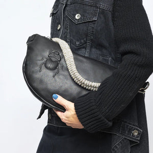 The GANRIELE FRANTZEN - SCARAB LEATHER XL BELT BAG IN BLACK WITH EXTRA CRYSTAL STRAP by GABRIELE FRANTZEN is a black leather, crescent-shaped crossbody bag featuring a long black strap and an extra decorative crystal handle, displayed against a plain white background.