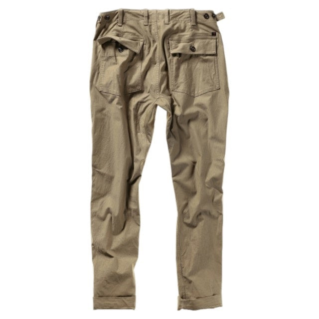 The RELWEN Supply Pant in Worker Khaki is a pair of light brown chinos inspired by classic military utility pant design, featuring side adjuster tabs, a button fly, broken twill fabric, and cuffs at the ankles with a subtly tapered leg silhouette—laid flat on a white background.