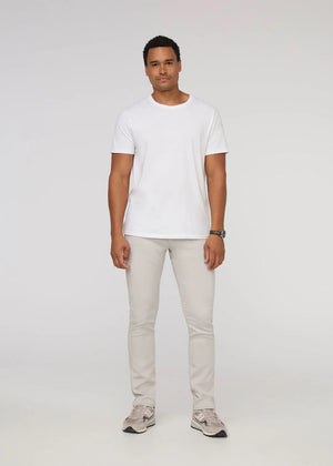 A person stands facing forward on a plain light background, wearing DUER NO SWEAT ATHLETIC TAPER PANTS IN MIST and matching light gray sneakers, feet slightly apart.