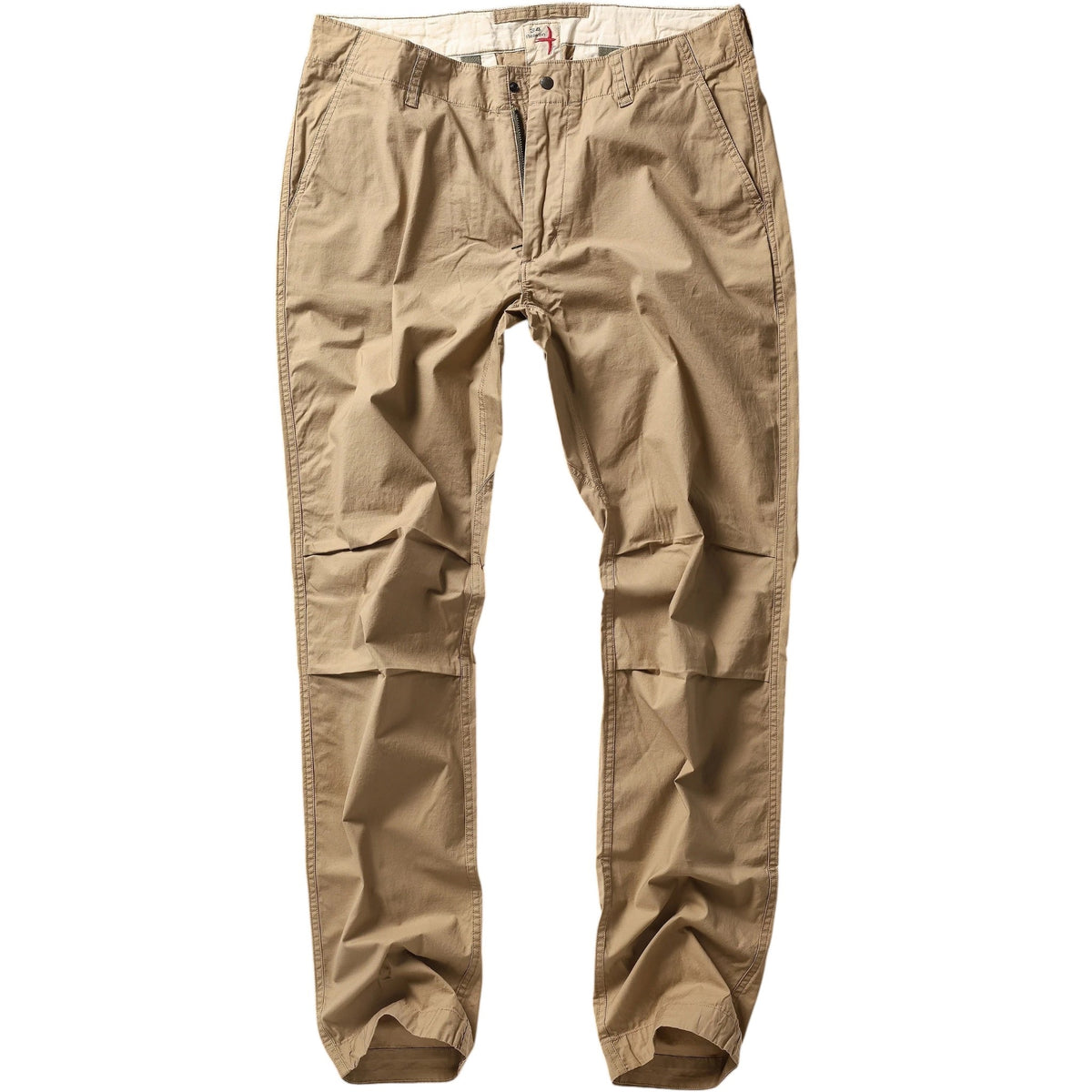Wearing RELWEN's Flyweight Flex Chino in British Khaki, a person stands on a beachside boardwalk near a weathered bench, with flip-flops and a plaid shirt, seashells and sand in the background.