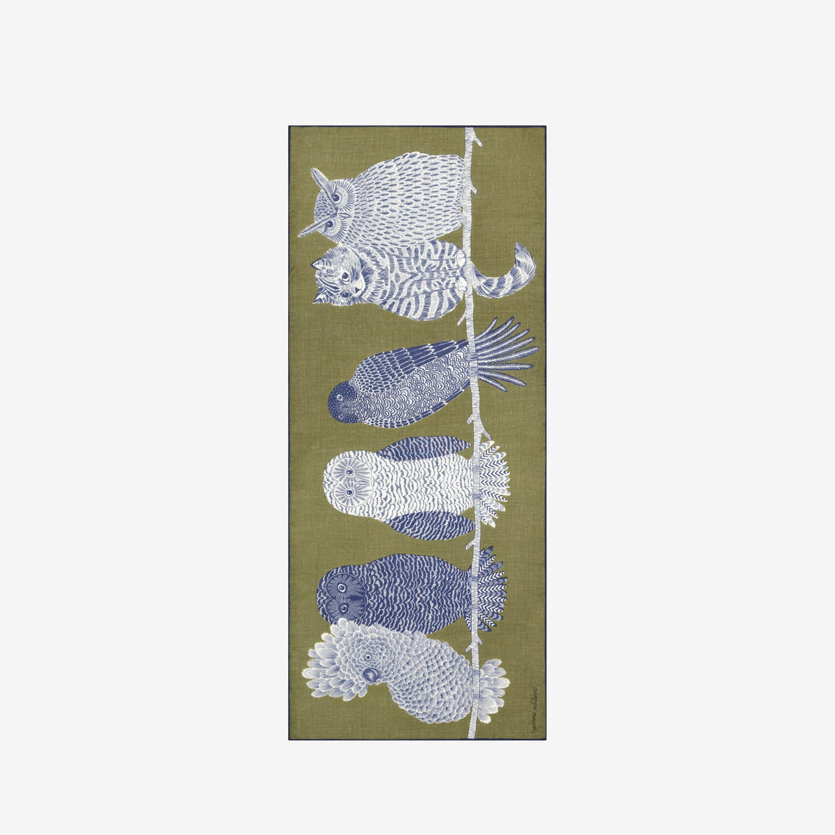A woman with blond hair tied back wears a light gray sweater and black pants, with the INOUI EDITIONS - CHOUETTE WOOL SCARF by INOUI—an olive green wool scarf featuring a large blue and white owl design—draped over her shoulder. This hand-printed scarf, made in India, adds a vibrant touch against the plain white background.