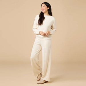 A woman wears a SOFTIES - DREAMTECH BOAT NECK WITH PINTUCK PANT SET in olive green, featuring a long-sleeve boat neck top and matching wide-leg pintuck pants.