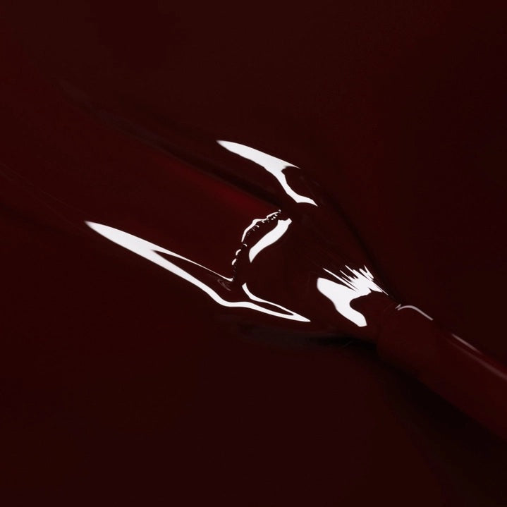 A bottle of MANUCURIST INC GREEN™ Nail Polish in the shade Hollyhock, featuring a dark burgundy color and a black cap.