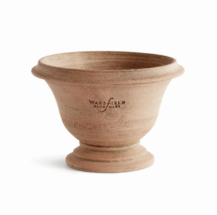 The NAPA HOME AND GARDEN - WAKEFIELD HANDMADE ASTON POT, crafted from aged terracotta with a wide rim and round base, sits on a stone surface beside another decorative planter in the background.