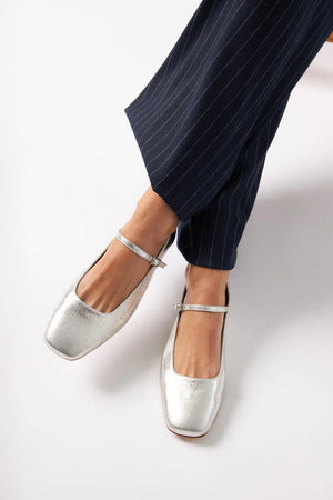 The AUGUSTA - JULIETA MARY JANE by AUGUSTA is a black leather flat shoe featuring a slender, adjustable strap across the top and a low wooden heel. With its renewed silhouette, slightly pointed toe, and minimalist design, this handcrafted Spanish shoe is presented against a plain, light gray background.