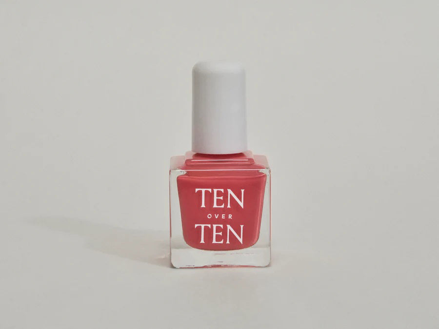 A glass bottle of TENOVERTEN - NAIL POLISH from the brand TEN OVER TEN, featuring a white cap and a dusty pink nail color. The front label displays "TEN OVER TEN" in white uppercase letters. This vegan, eight-free formula ensures both beauty and peace of mind. The background is plain and light-colored.