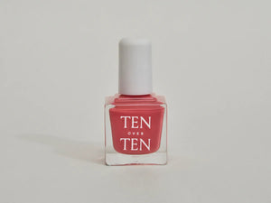 A glass bottle of TENOVERTEN - NAIL POLISH from the brand TEN OVER TEN, featuring a white cap and a dusty pink nail color. The front label displays "TEN OVER TEN" in white uppercase letters. This vegan, eight-free formula ensures both beauty and peace of mind. The background is plain and light-colored.