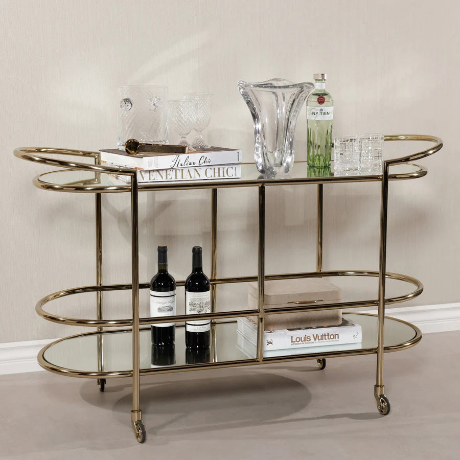 The ZODAX CONSOLE BAR CART showcases a minimalistic design with a shiny gold metal frame, mirrored shelves, curved corners, and clean lines—making it a stylish serving station for any modern space.