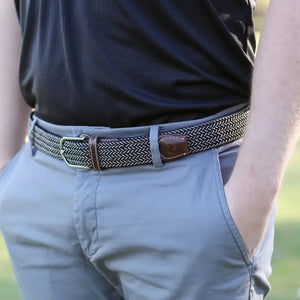 The ROOSTAS - MAUI WOVEN STRETCH BELT by ROOSTAS features a black and white zigzag pattern, brown leather ends, a silver buckle, and an adjustable clasp for the perfect fit.