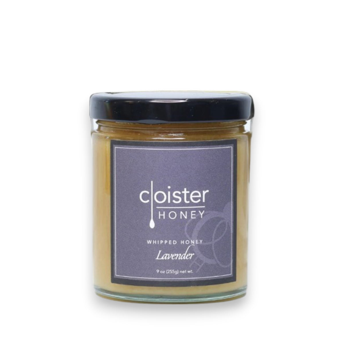 Cloister Honey's Whipped Lavender Honey 9oz brings a touch of France with its lavender essence. The clear jar with a black lid showcases creamy light brown honey, complemented by a minimalist label adorned with elegant floral graphics.