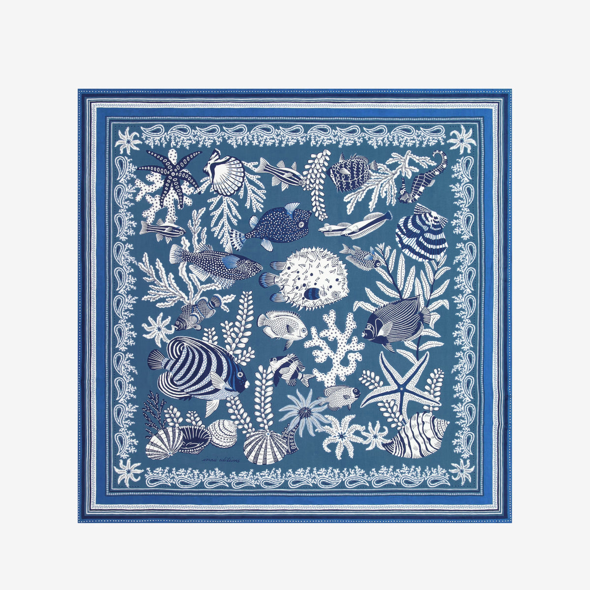 A person in a sleeveless cream top wears the INOUI EDITIONS - NEPTUNE SCARF IN BLUE by INOUI, featuring white floral and geometric patterns, draped over one shoulder against a plain white background.