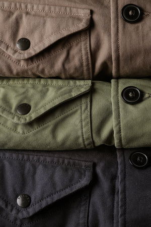 The RELWEN Pile-Lined Chore Coat in Palm Green is a stylish workwear jacket with a green quilted sleeve, olive-green collar and cuffs, and a soft gray fleece body with rugged lining, shown lying open on a white background.