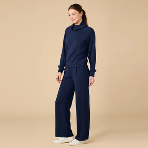 A woman seen from behind wearing the fuchsia SOFTIES - DREAMTECH COWL NECK WITH PLEATED PANT set featuring a long-sleeved cowl neck top and matching pleated pants.