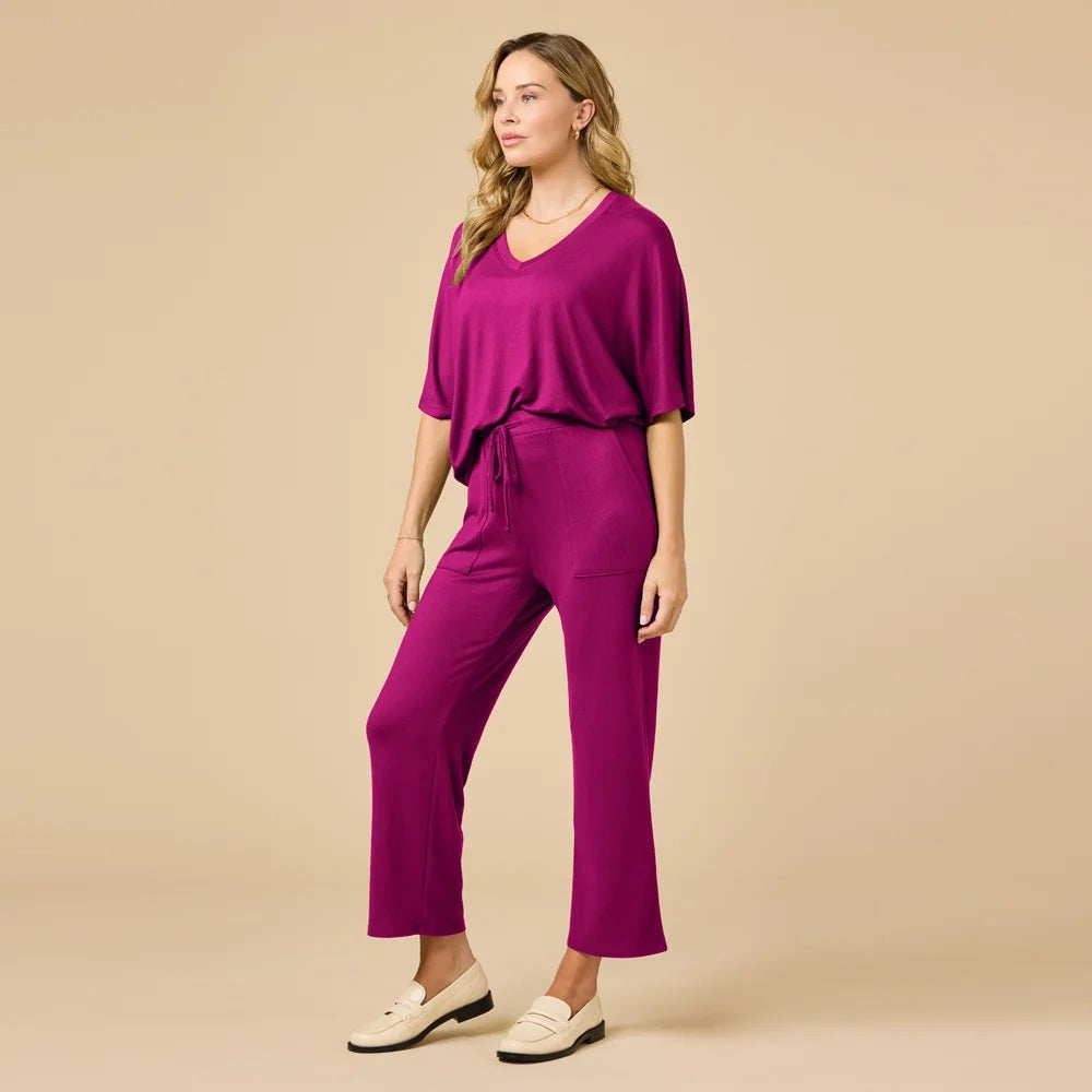 A woman wears a SOFTIES - DREAM RELAXED V-NECK WITH CAPRI LOUNGE SET in magenta, featuring a V-neck top with elbow-length sleeves and matching cropped drawstring pants, paired with cream-colored loafers.