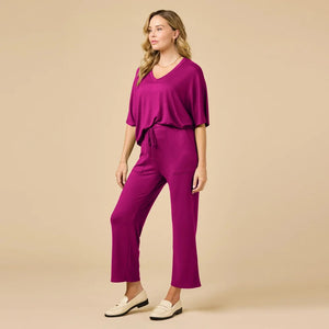 A woman wears a SOFTIES - DREAM RELAXED V-NECK WITH CAPRI LOUNGE SET in magenta, featuring a V-neck top with elbow-length sleeves and matching cropped drawstring pants, paired with cream-colored loafers.