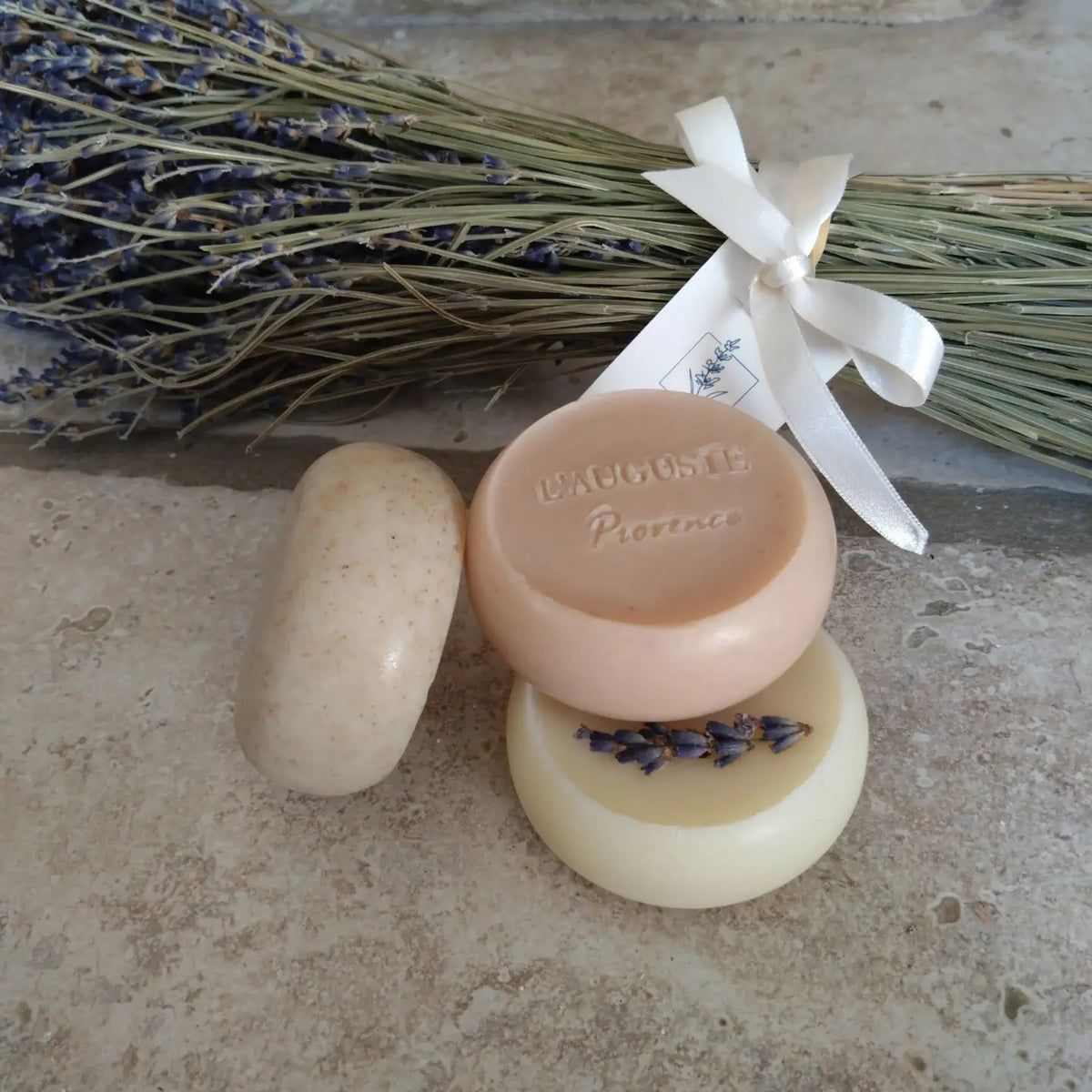 The L’AUGUSTE PROVENCE Set of Handcrafted French Soaps features three round soaps in a white box, with the left soap topped with dried lavender—an elegant Provence-inspired gift set.