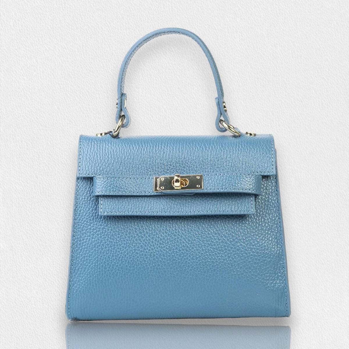 The LE BORSETTE LEATHER SATCHEL BAG is a small, structured satchel-shaped handbag in light pink, featuring a gold clasp at the front. It boasts a single top handle, an adjustable shoulder strap, and two gold-tone hardware pieces on either side of the handle. The textured leather adds to its luxurious and elegant appearance against the plain white background.