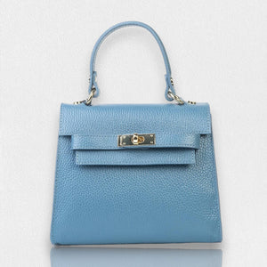 The LE BORSETTE LEATHER SATCHEL BAG is a small, structured satchel-shaped handbag in light pink, featuring a gold clasp at the front. It boasts a single top handle, an adjustable shoulder strap, and two gold-tone hardware pieces on either side of the handle. The textured leather adds to its luxurious and elegant appearance against the plain white background.