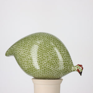 A LES CERAMIQUES DE LUSSAN - PECKING CERAMIC FRENCH GUINEA IN GREEN SPECKLED WHITE figurine, crafted in the signature style of LES CERAMIQUES DE LUSSAN, featuring a green and white speckled pattern and standing on a cylindrical white base against a plain background.
