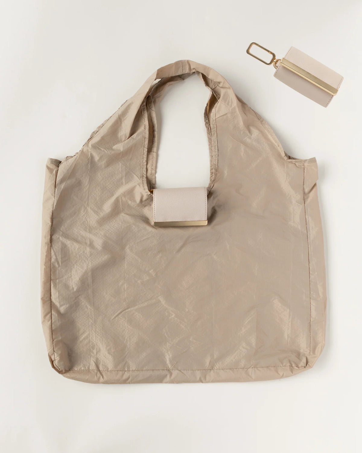The KEOTE - KEYCHAIN TOTE IN STONE by KEOTE is a beige, lightweight, crinkled tote laid flat, with a matching rectangular pouch and keychain attachment shown above for easy storage of the reusable bag.