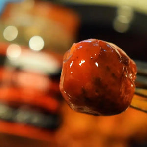 A person brushes savory barbecue sauce onto the burgers sizzling on the grill, holding a jar of CACKALACKY - CHEERWINE SWEET SAUCE in their other hand. This scene of Southern cuisine unfolds against the backdrop of a grassy outdoor setting.