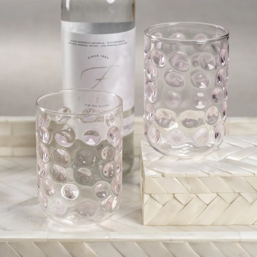 Five **AIRELLES GLASS TUMBLERS** by **ZODAX**, adorned with textured bubble patterns and distinct colored accents in blue, green, amber, clear, and pink. Each glass boasts a 460 ml capacity and is elegantly displayed on a light-colored fabric surface against a neutral background.