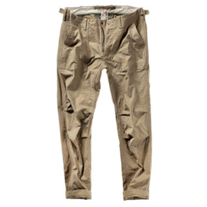 The RELWEN Supply Pant in Worker Khaki is a pair of light brown chinos inspired by classic military utility pant design, featuring side adjuster tabs, a button fly, broken twill fabric, and cuffs at the ankles with a subtly tapered leg silhouette—laid flat on a white background.