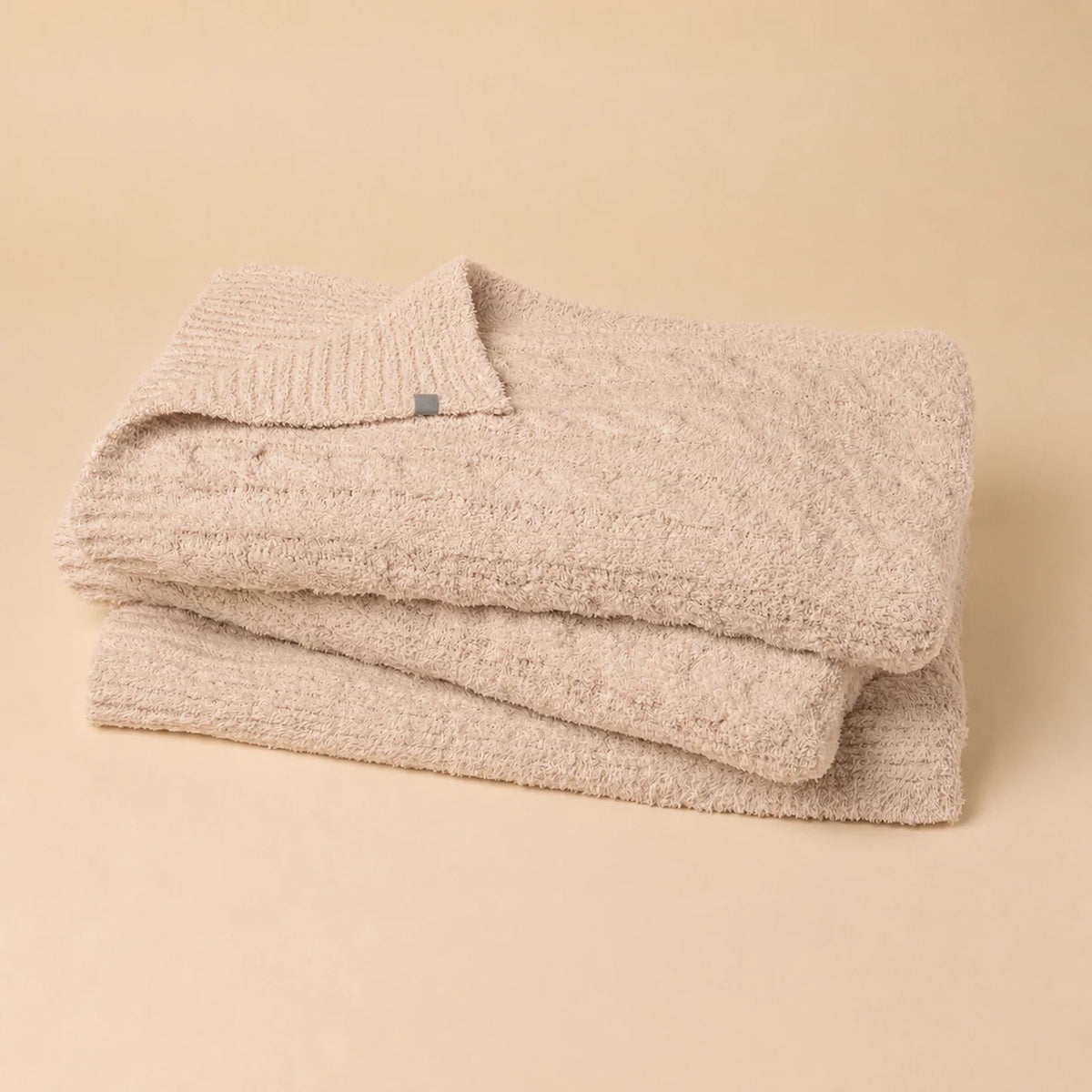 Folded off-white SOFTIES - CABLE KNIT MARSHMALLOW BLANKET tied with a branded ribbon.