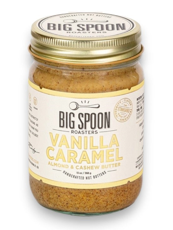 A jar of BIG SPOON ROASTERS - VANILLA CARAMEL ALMOND &amp; CASHEW BUTTER. The jar features a gold lid and a cream-colored label with black and yellow text. The label includes the product name, the phrase &quot;handcrafted nut butters,&quot; and mentions organic cashews. The net weight is 13 oz (368g).