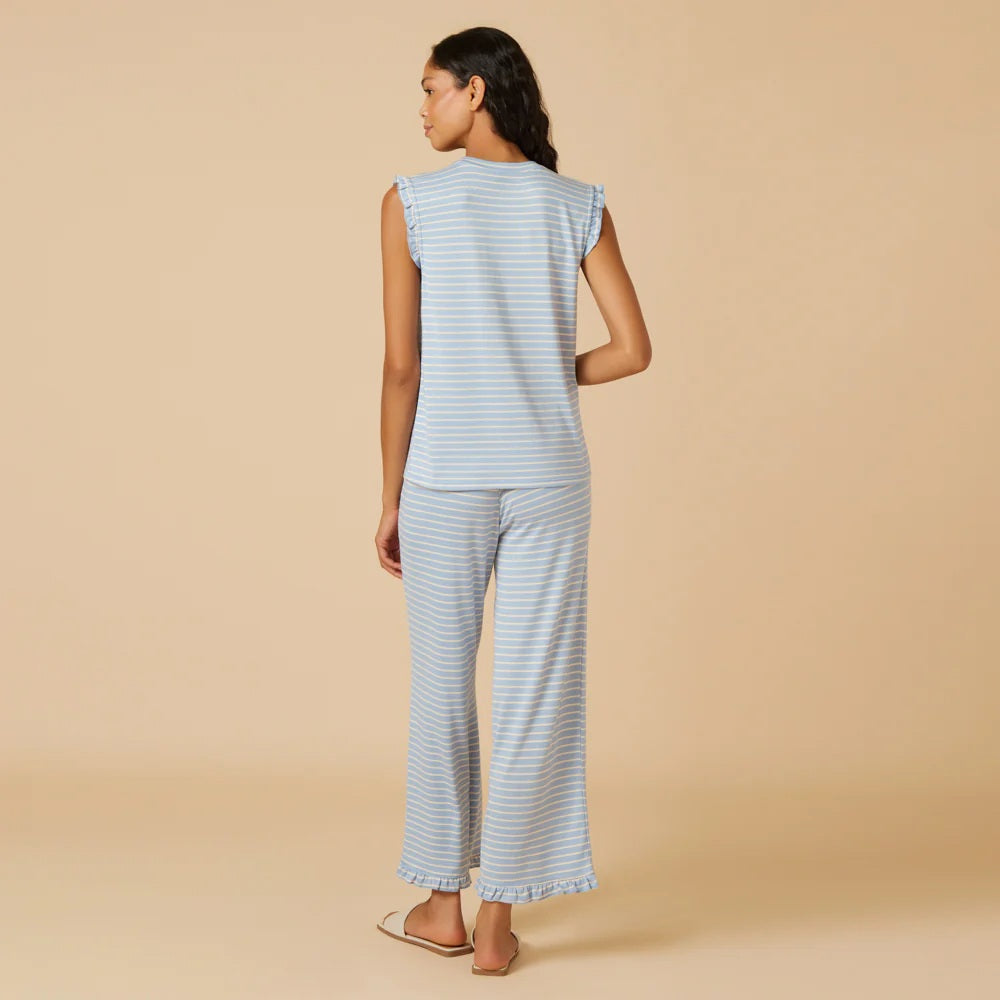 A woman with long dark hair wears the SOFTIES Dream Ruffle V-Neck with Cropped Pant in Sky Blue Stripe as she looks off to the side against a beige background.