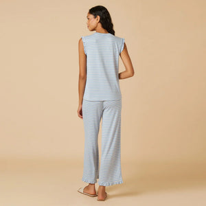 A woman with long dark hair wears the SOFTIES Dream Ruffle V-Neck with Cropped Pant in Sky Blue Stripe as she looks off to the side against a beige background.