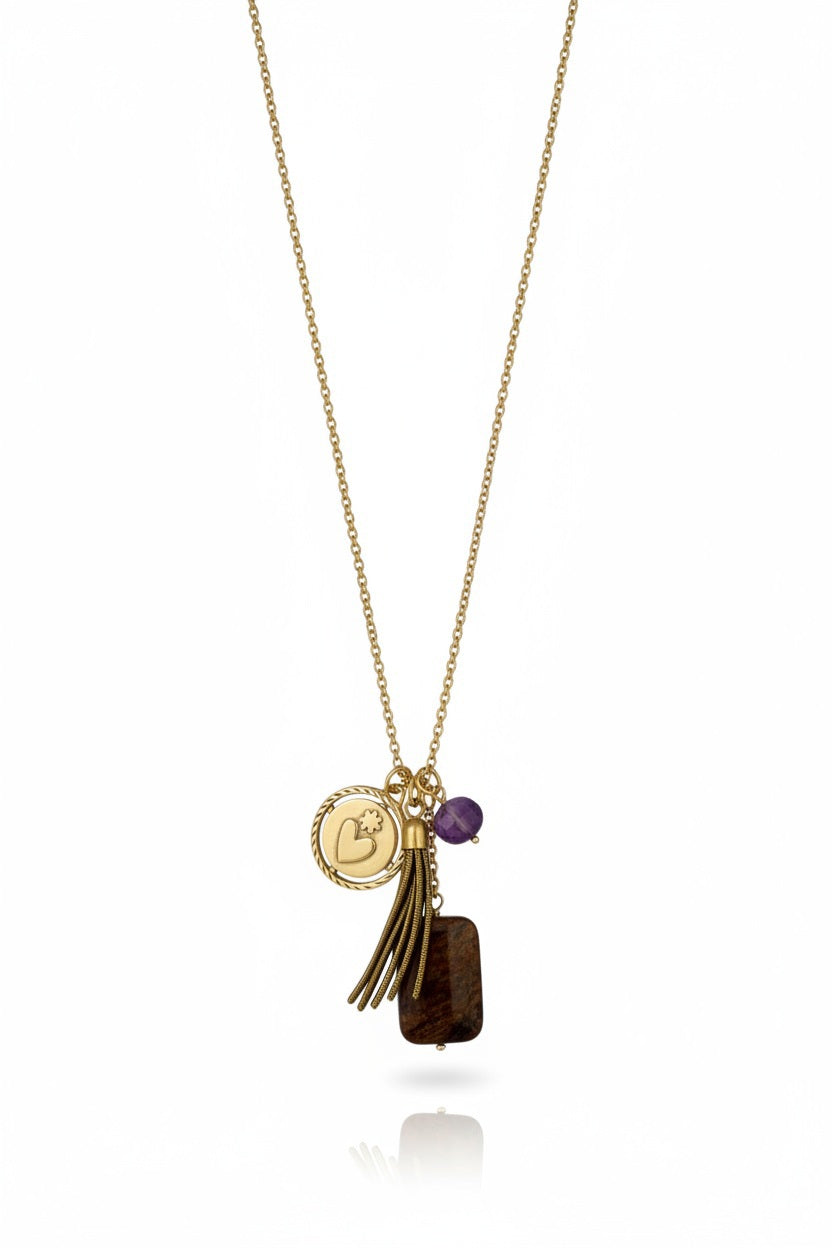 The SANDRINE FRANCE STUDIO DONATA Necklace features four charms—a round disc with a heart, a small gold tassel, an amethyst pendant bead, and a rectangular bronzite stone—suspended from a delicate gold chain. Handmade in NYC by SANDRINE FRANCE STUDIO, this unique bronzite necklace is shown against a white background.