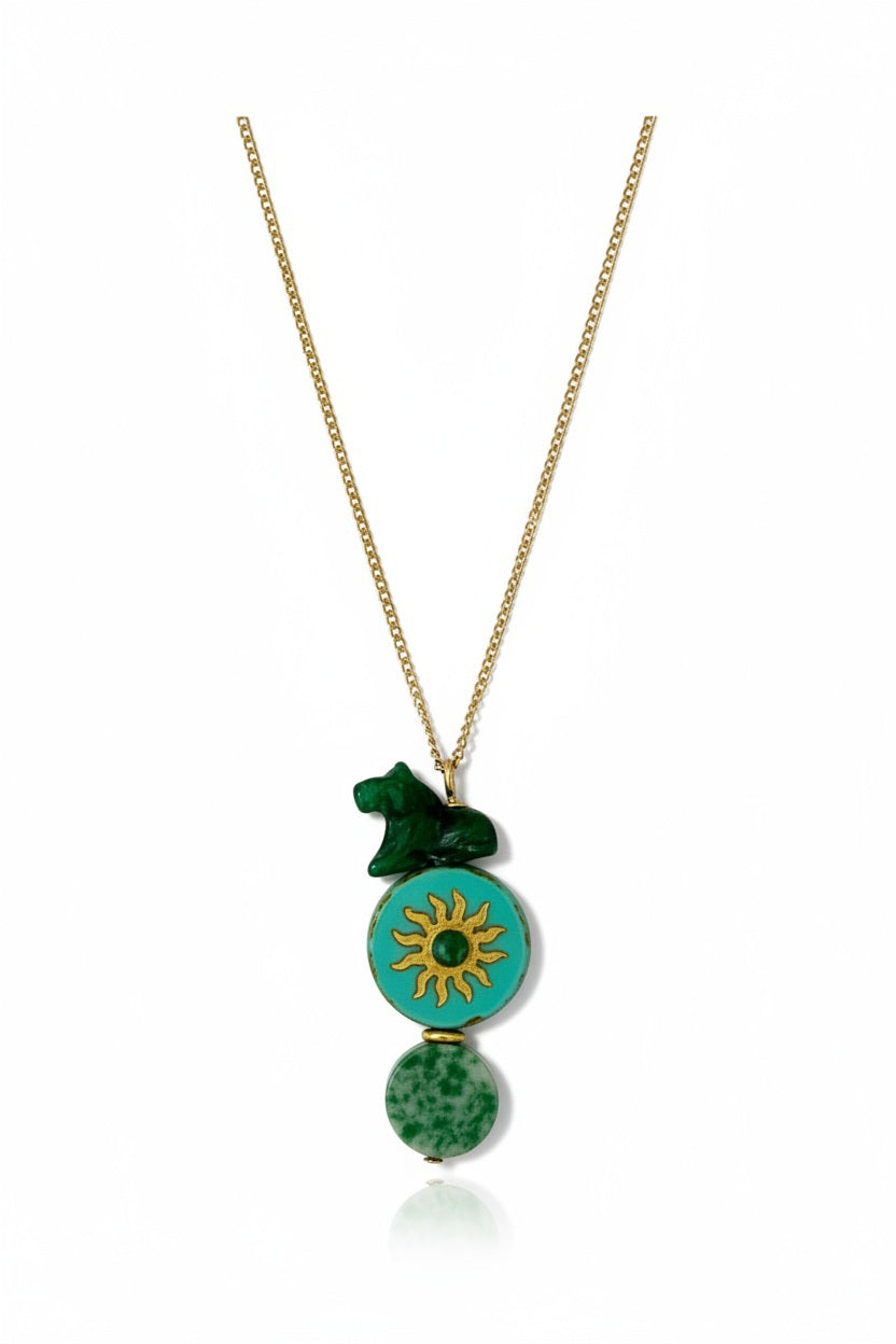 The SANDRINE FRANCE STUDIO - COMPANION AUSTIN NECKLACE by SANDRINE FRANCE STUDIO features a gold chain adorned with three green pendants: a small abstract shape, a jade round disk accented with a gold sun motif, and an oval bead with a marbled pattern—each detail showcasing the artistry of handmade NYC craftsmanship.