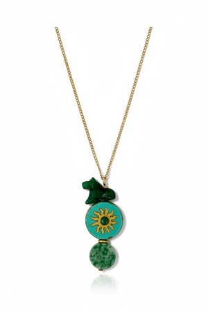 The SANDRINE FRANCE STUDIO - COMPANION AUSTIN NECKLACE by SANDRINE FRANCE STUDIO features a gold chain adorned with three green pendants: a small abstract shape, a jade round disk accented with a gold sun motif, and an oval bead with a marbled pattern—each detail showcasing the artistry of handmade NYC craftsmanship.