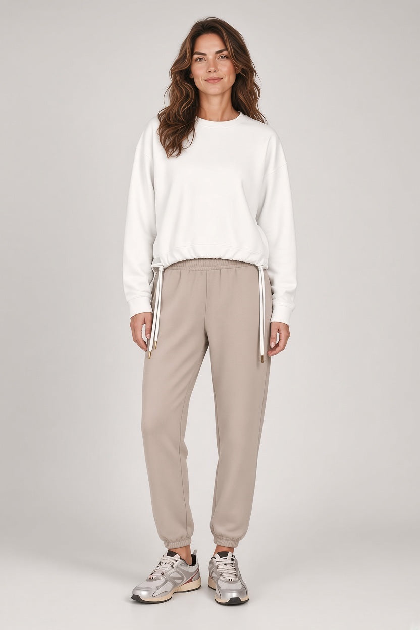 A person wears a SAVE THE DUCK - AKEMI SWEATER IN CLOUD WHITE, a soft-touch crewneck sweatshirt with adjustable lycra cords at the hem, paired with tan sweatpants.