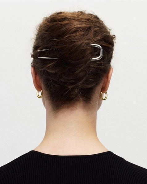 The MACHETE - MIDI FRENCH HAIR PIN IN GOLD by MACHETE is a handcrafted, U-shaped hair accessory with two long, pointed prongs, standing vertically against a plain white background to highlight its elegant simplicity.