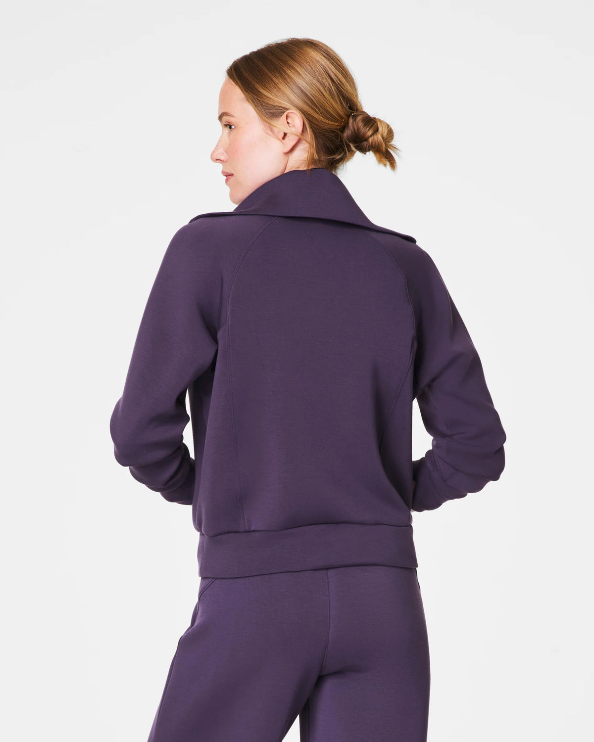 A person with short hair is wearing a SPANX AIRESSENTIALS HALF ZIP sweater in navy blue, made from lightweight spacer fabric, paired with black pants. Their arms are crossed over their chest as they stand against a plain, light grey background.